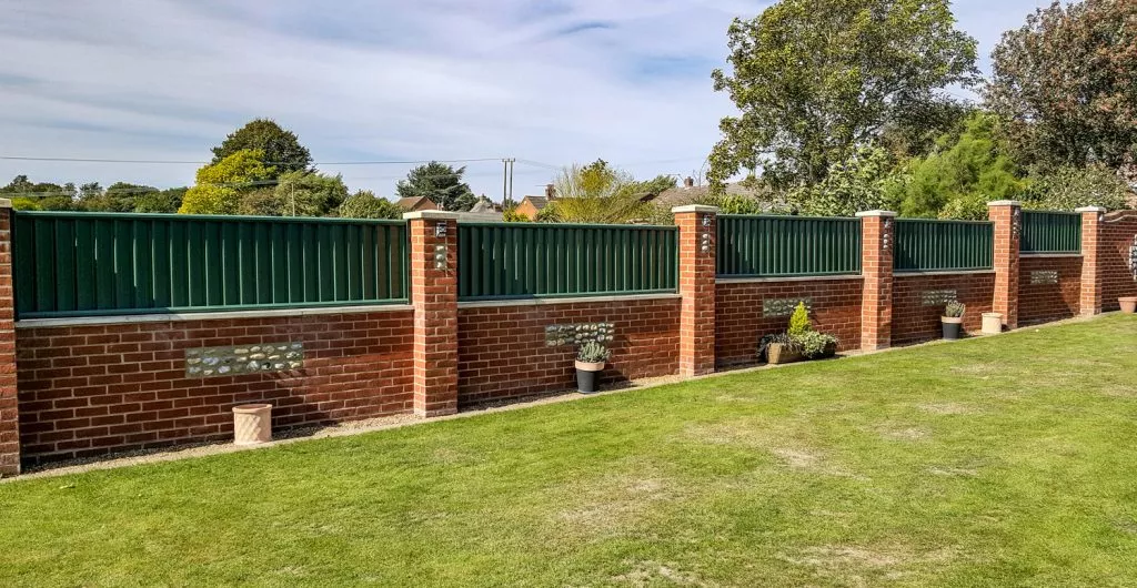Green steel fence on top of brick wall